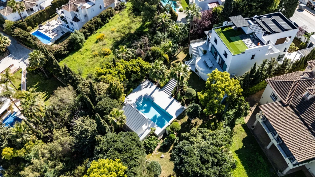 Drone view of a white modern villa with a rooftop terrace and a garden pool in Nueva Andalucía, Marbella