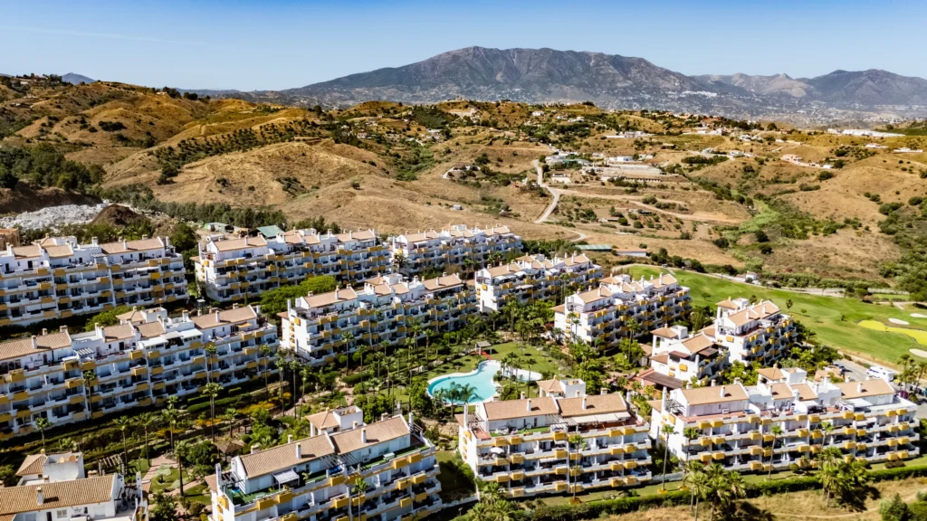 Drone photo of apartments beside a golf course with mountains behind