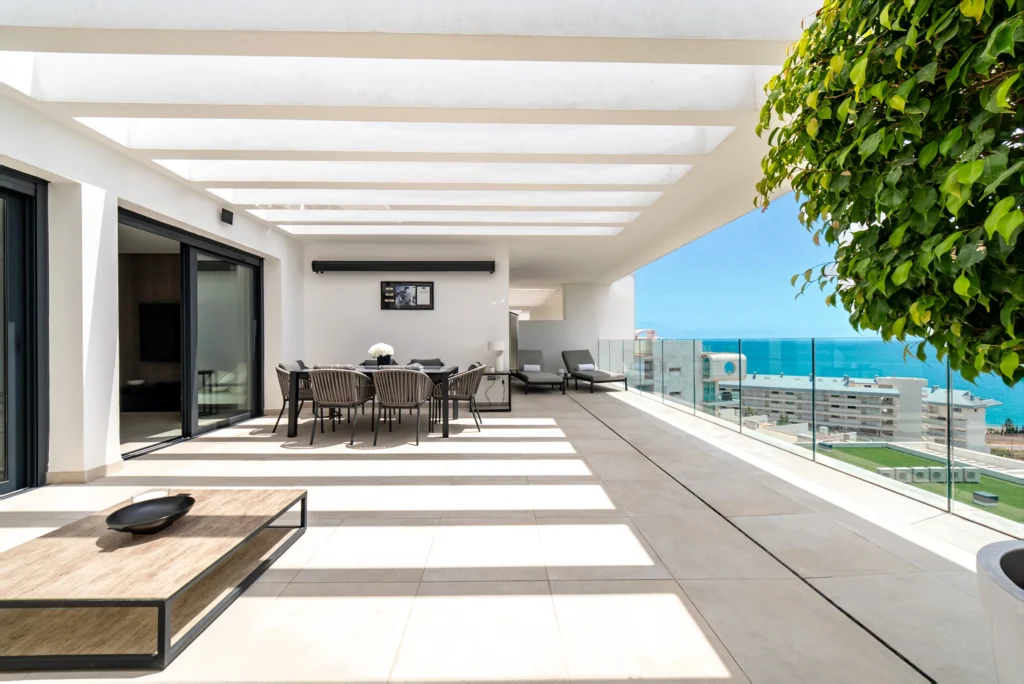 Wide terrace under a slatted pergola looking out to the sea